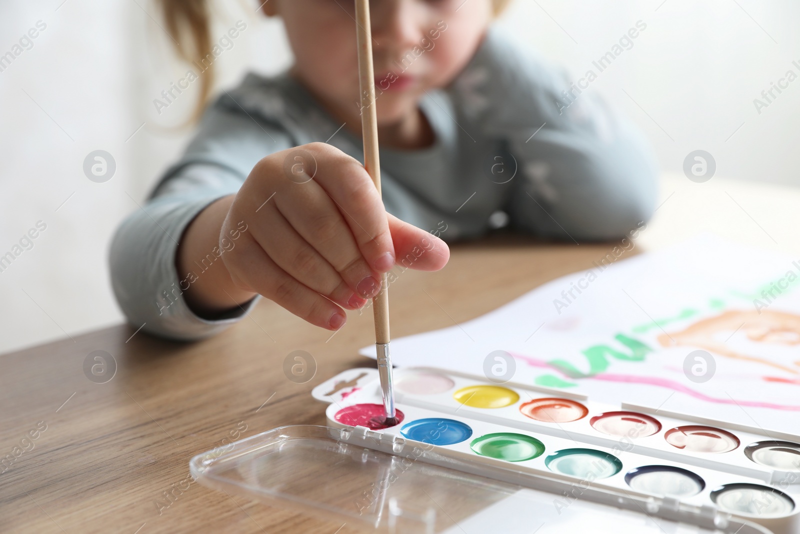 Photo of Little girl with brush drawing at wooden table indoors, selective focus. Child`s art