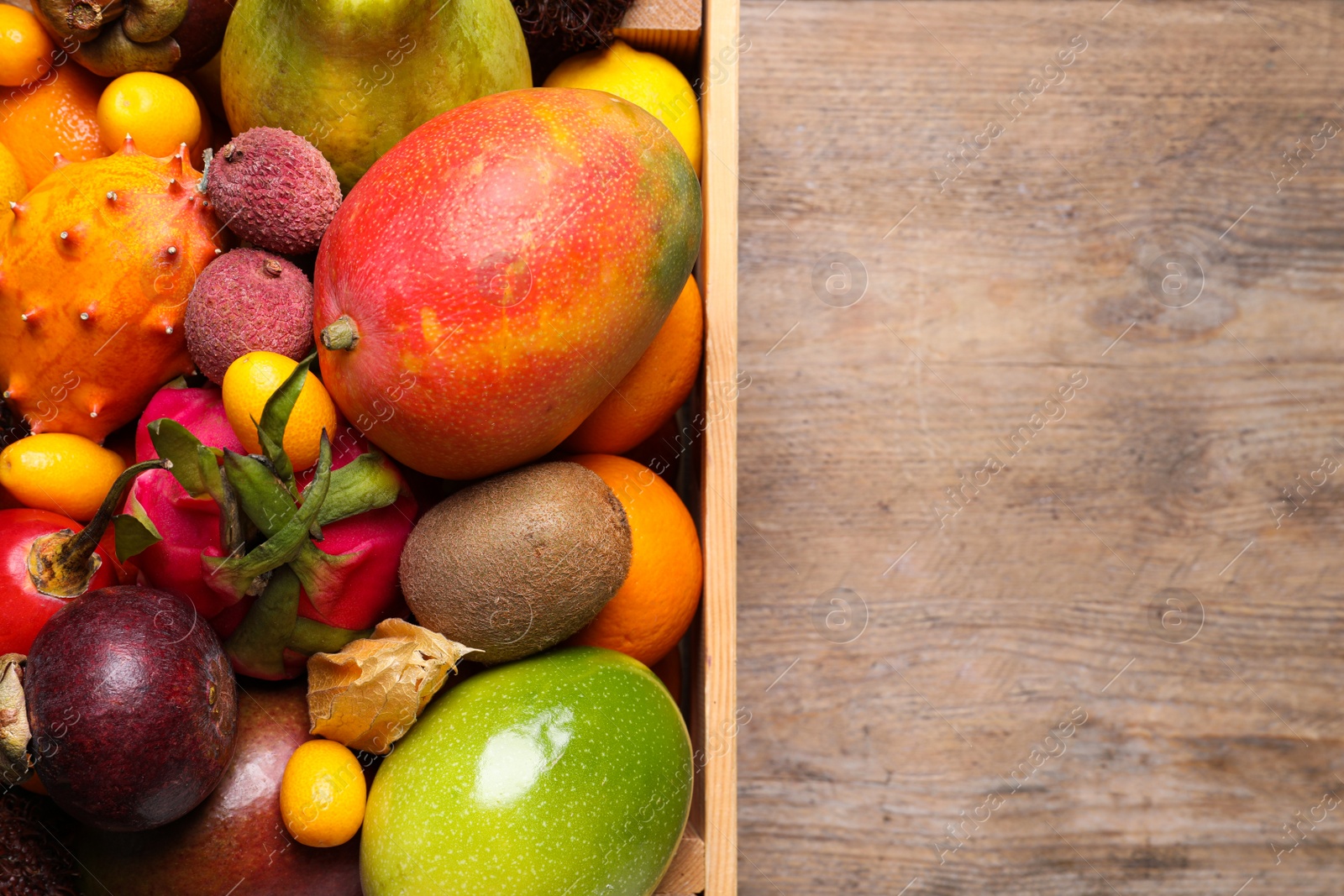 Photo of Crate with different exotic fruits on wooden table, top view. Space for text