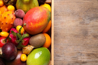Crate with different exotic fruits on wooden table, top view. Space for text