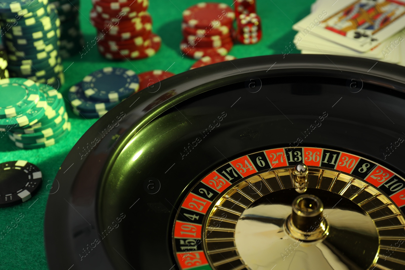 Photo of Roulette wheel with ball, playing cards and chips on green table, closeup. Casino game