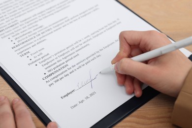 Woman signing contract at wooden table, closeup.