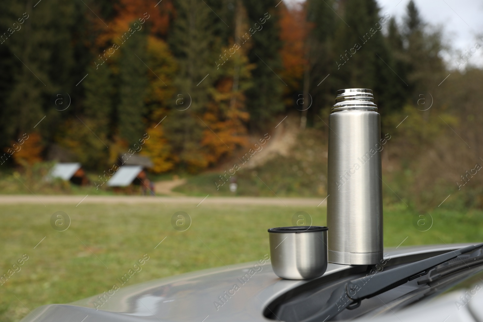 Photo of Metallic thermos and cup lid on car trunk outdoors, space for text