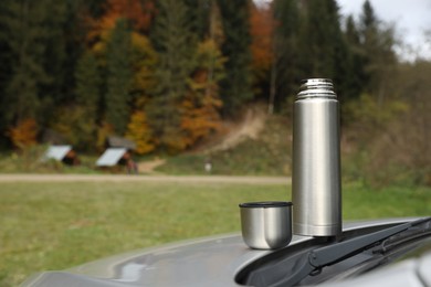 Photo of Metallic thermos and cup lid on car trunk outdoors, space for text