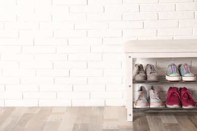 Photo of Shoe storage bench with different sneakers near brick wall, space for text