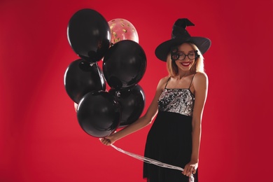 Beautiful woman in witch costume with balloons on red background. Halloween party