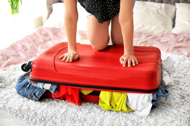 Photo of Young woman struggling to close suitcase on bed