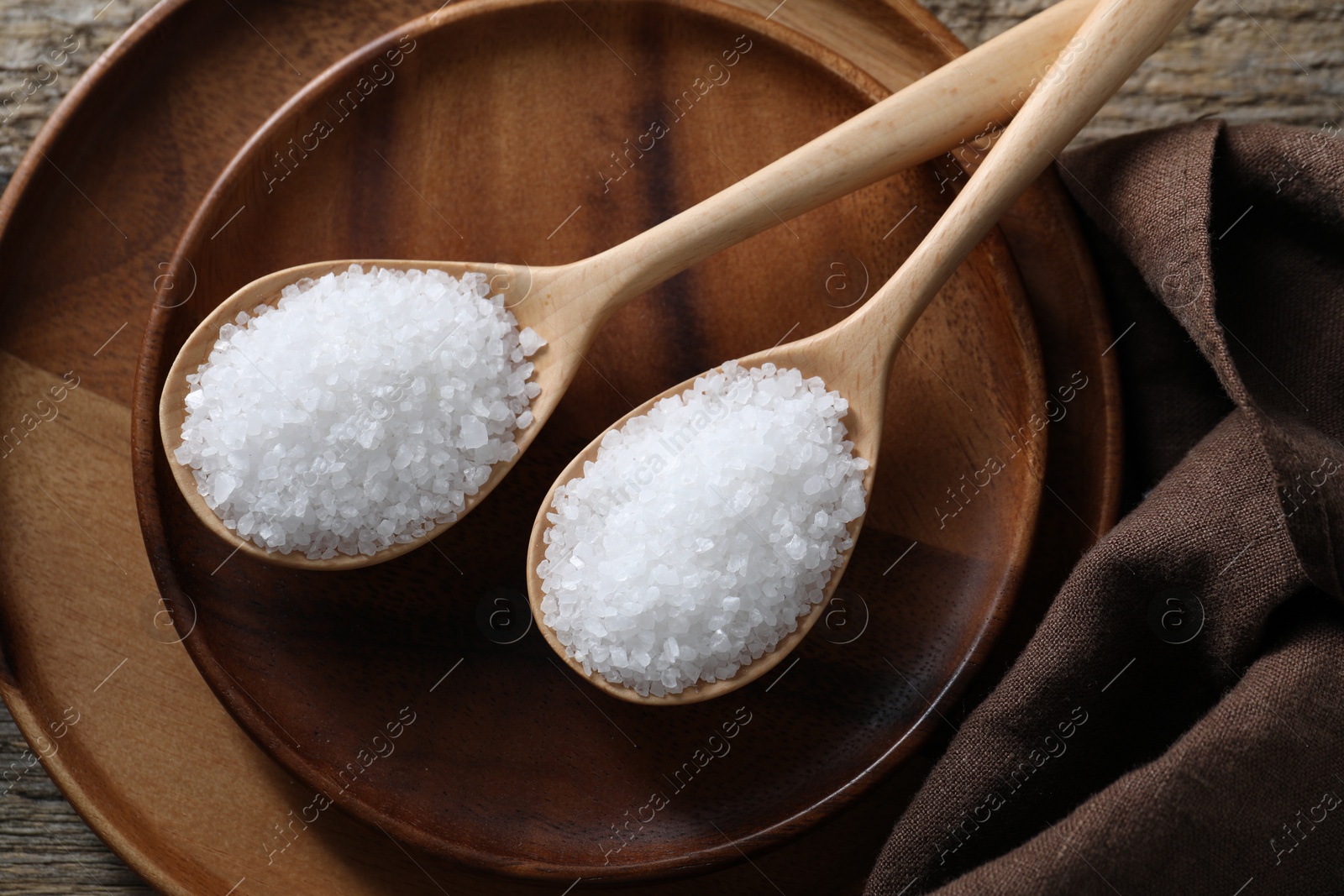 Photo of Organic salt in spoons on wooden table, top view