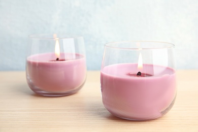 Burning wax candles in glass holders on wooden table