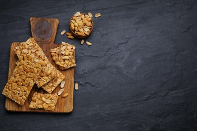 Photo of Delicious peanut bars (kozinaki) and ingredients on black table, flat lay. Space for text