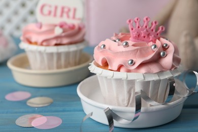 Photo of Delicious cupcakes with pink cream and toppers for baby shower on light blue wooden table, closeup
