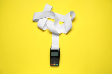 Photo of Payment terminal with thermal paper for receipt on yellow background, top view