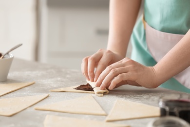 Woman preparing tasty croissants with chocolate paste on table, closeup