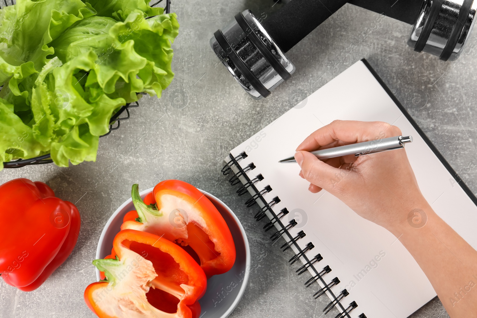 Photo of Woman developing diet plan at grey table with products and dumbbells, top view