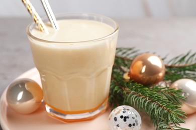 Photo of Glass of delicious eggnog and decorated fir branch on gray table, closeup