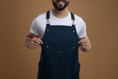 Photo of Smiling man in kitchen apron on brown background, closeup. Mockup for design