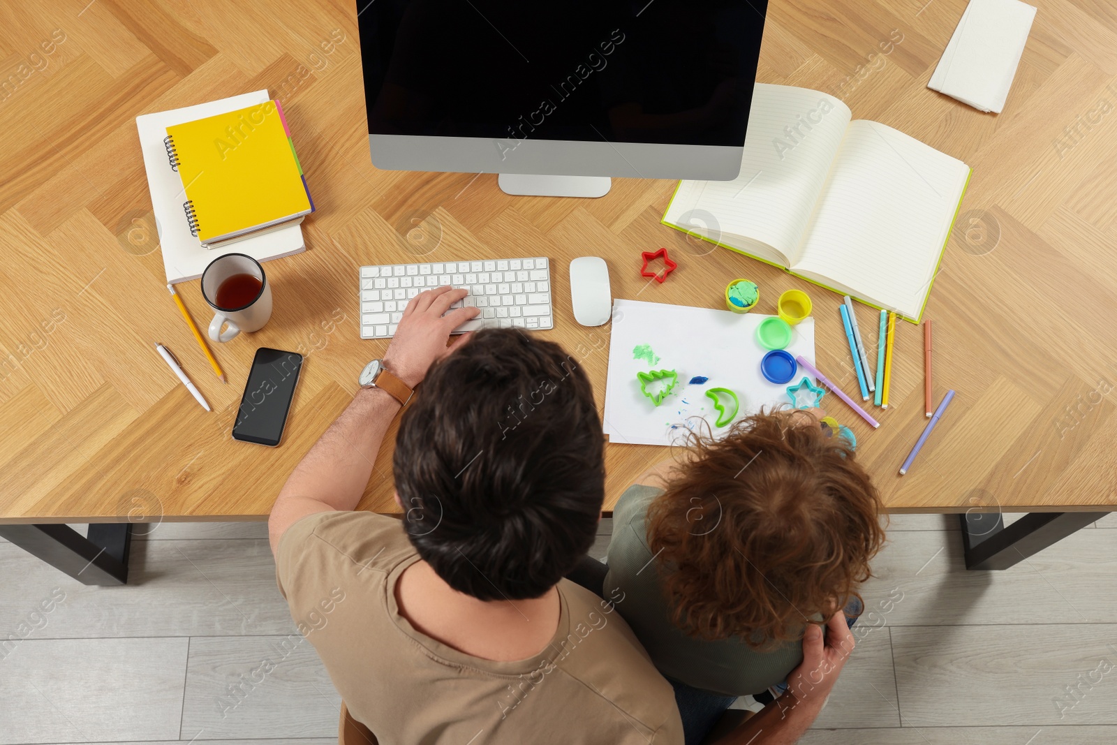 Photo of Man working remotely at home. Father and his son at desk with computer, top view