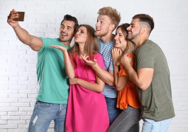 Photo of Happy young people taking selfie near white brick wall