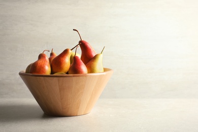 Bowl with ripe pears on table against light background. Space for text