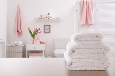 Stack of fresh towels on light grey table in bathroom. Space for text