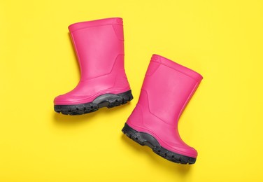 Photo of Pair of bright pink rubber boots on yellow background, top view