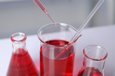 Photo of Laboratory analysis. Dripping red liquid into beaker on table, closeup