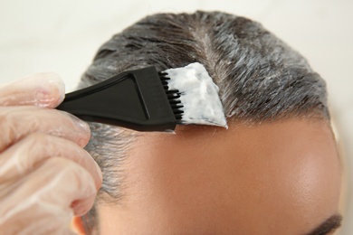 Young woman dyeing her hair against light background, closeup