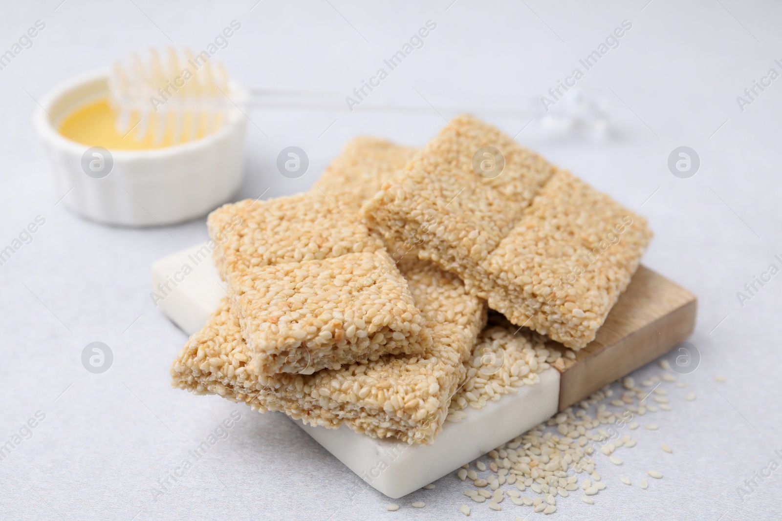 Photo of Delicious sesame kozinaki bars and honey on white table, closeup