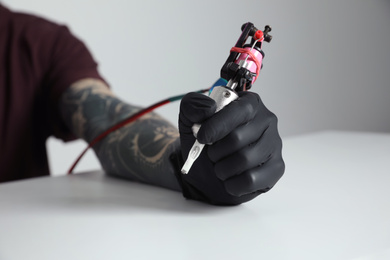 Photo of Tattoo artist with professional machine at table against light background, closeup