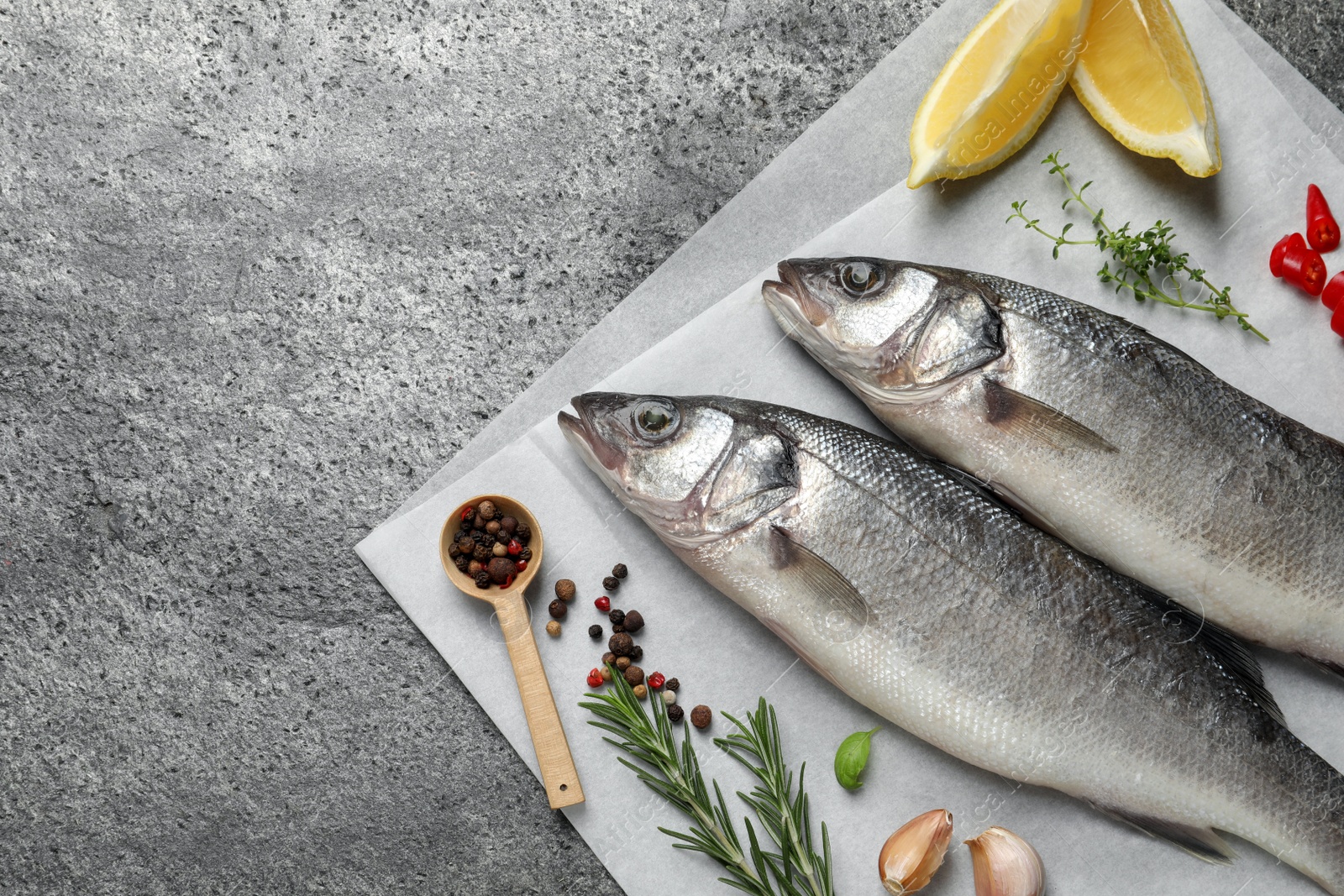 Photo of Sea bass fish and ingredients on grey table, above view. Space for text