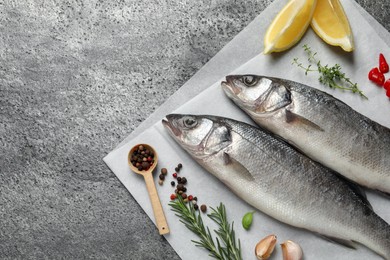 Photo of Sea bass fish and ingredients on grey table, above view. Space for text