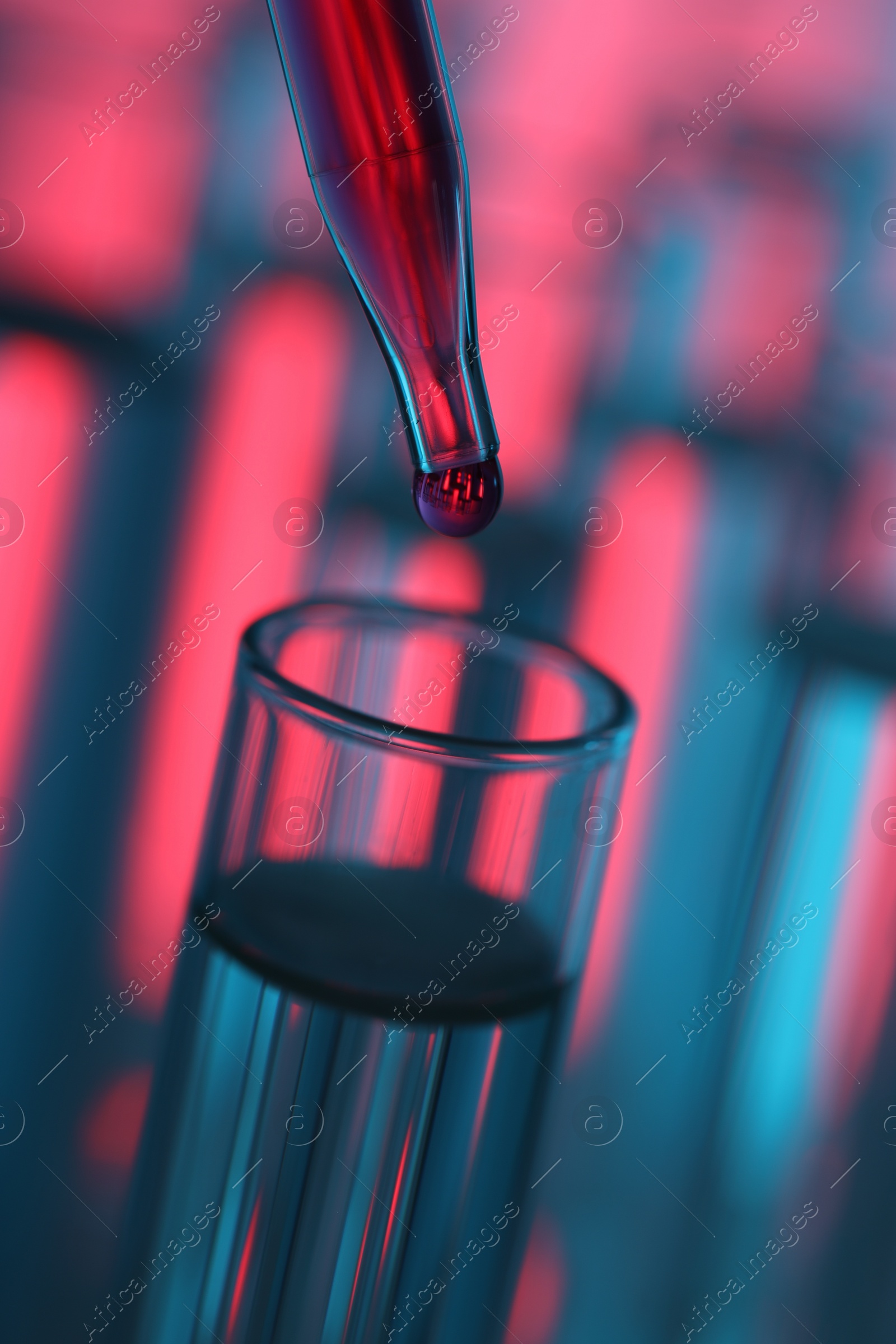 Photo of Dripping liquid from pipette into test tube on color background, closeup