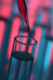 Photo of Dripping liquid from pipette into test tube on color background, closeup