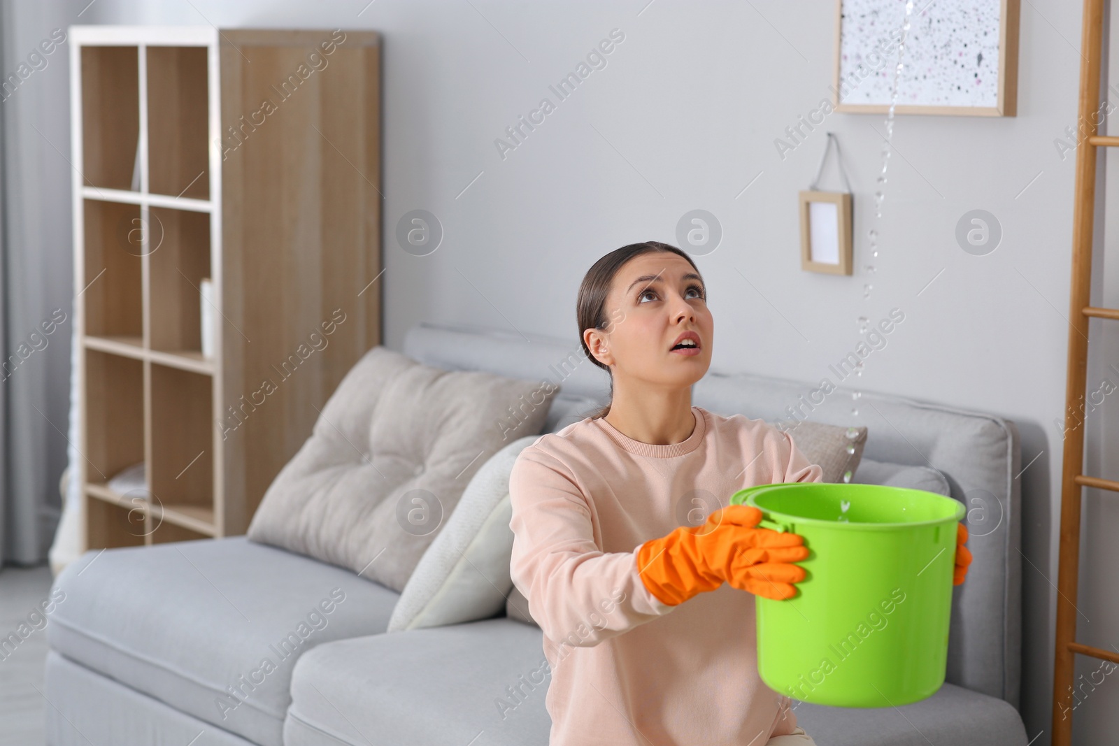 Photo of Young woman collecting leaking water from ceiling at home, space for text. Time to call roof repair service