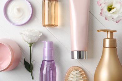 Flat lay composition with different hair products and flowers on white wooden table