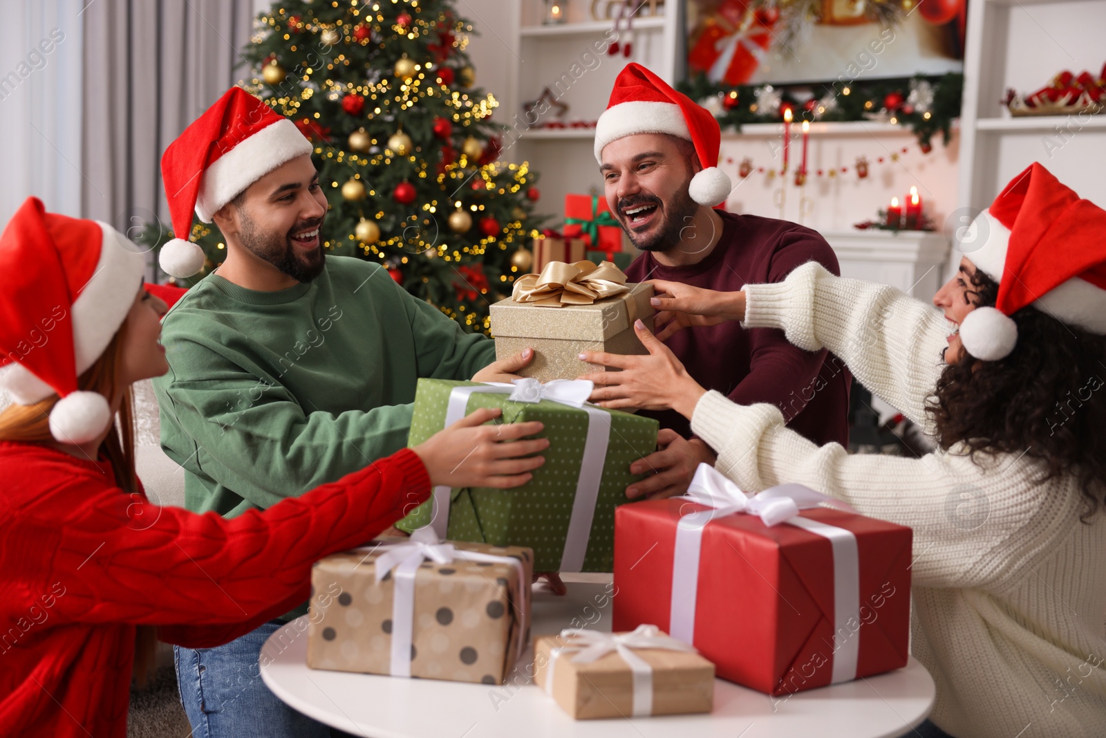 Photo of Christmas celebration. Happy friends in Santa hats exchanging gifts at home