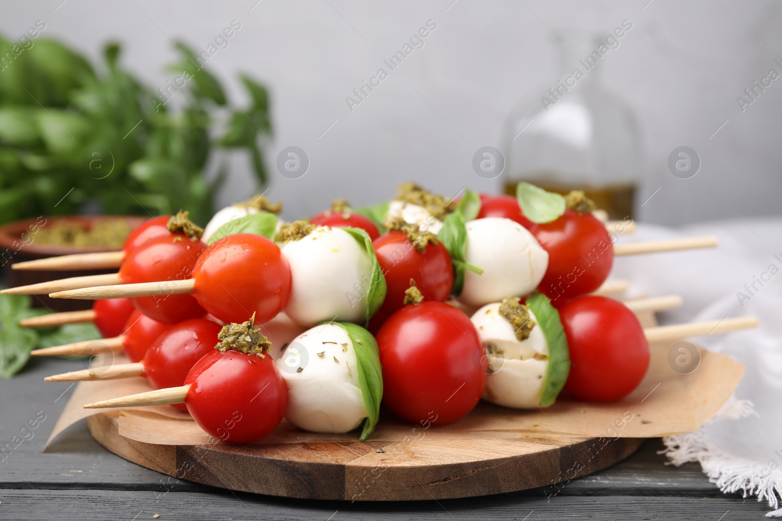 Photo of Caprese skewers with tomatoes, mozzarella balls, basil and pesto sauce on grey wooden table, closeup