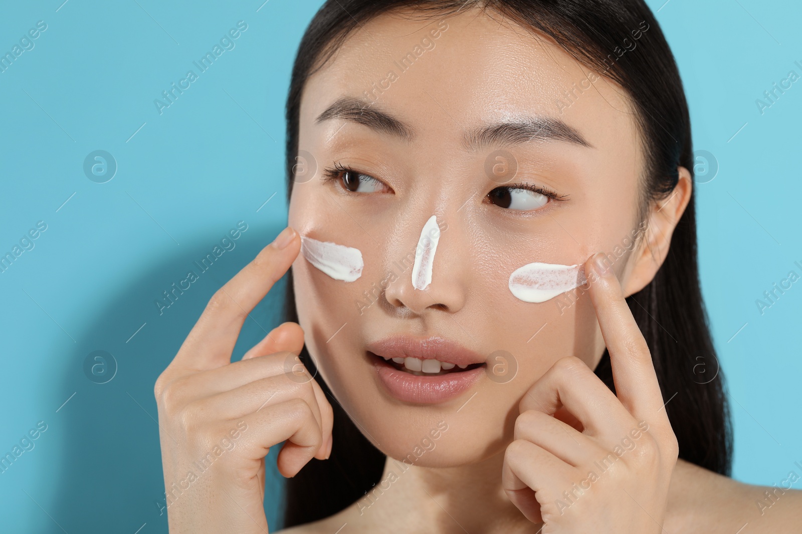 Photo of Beautiful young woman with sun protection cream on her face against light blue background. Space for text