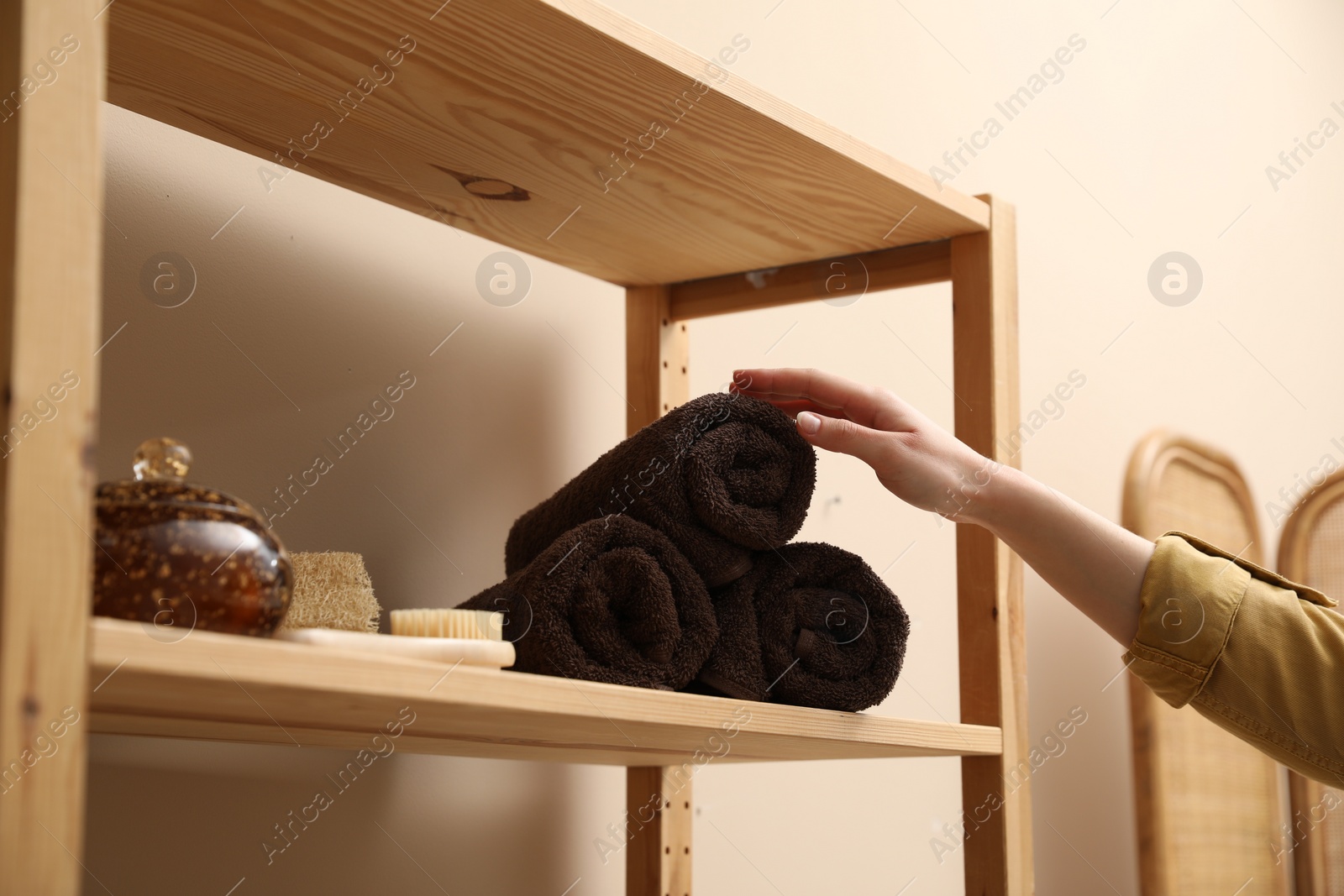 Photo of Woman taking rolled towel from shelf indoors, closeup