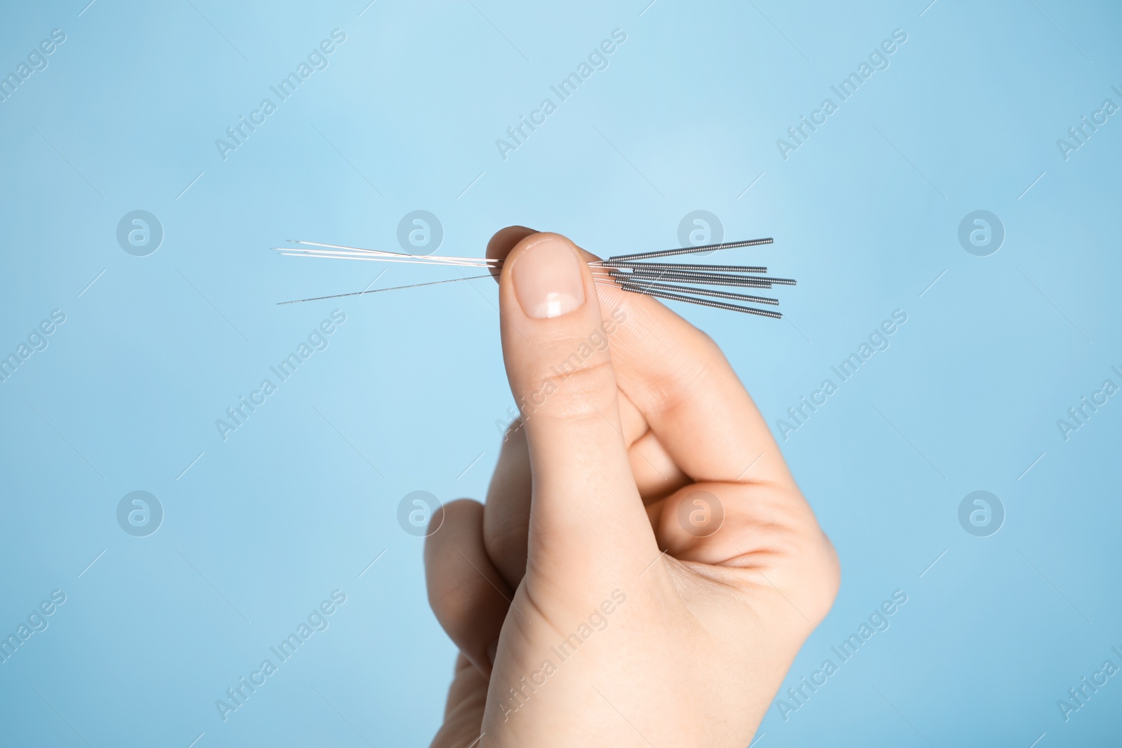 Photo of Woman holding needles for acupuncture on light blue background, closeup