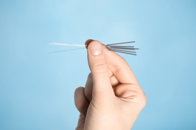 Woman holding needles for acupuncture on light blue background, closeup