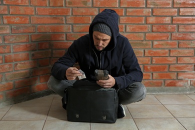 Photo of Drug dealer with narcotics sitting on floor against brick wall