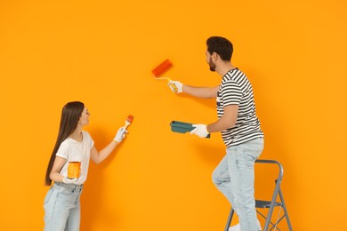 Photo of Designers painting orange wall with roller and brush