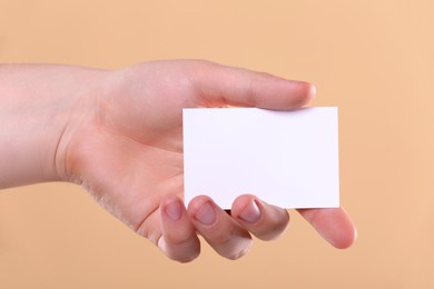 Man holding paper card on pale orange background, closeup. Mockup for design