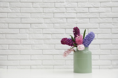 Photo of Beautiful hyacinths in metal can on table against brick wall, space for text. Spring flowers