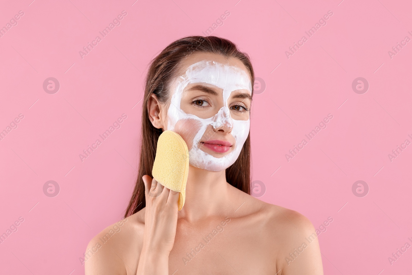 Photo of Happy young woman washing off face mask with sponge on pink background