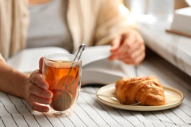 Photo of Woman with glass cup of tasty aromatic tea reading book at table, closeup