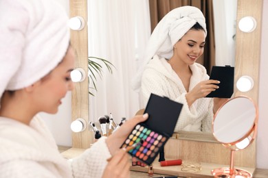 Photo of Beautiful woman applying makeup near mirror in room