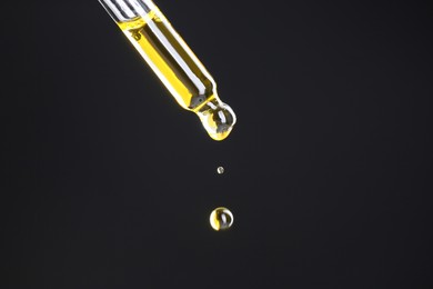 Photo of Dripping tincture from pipette on black background, closeup