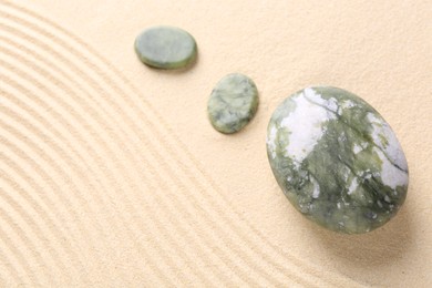 Photo of Zen garden stones on beige sand with pattern, above view. Space for text