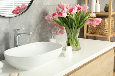 Vase with beautiful pink tulips and toiletries near sink in bathroom